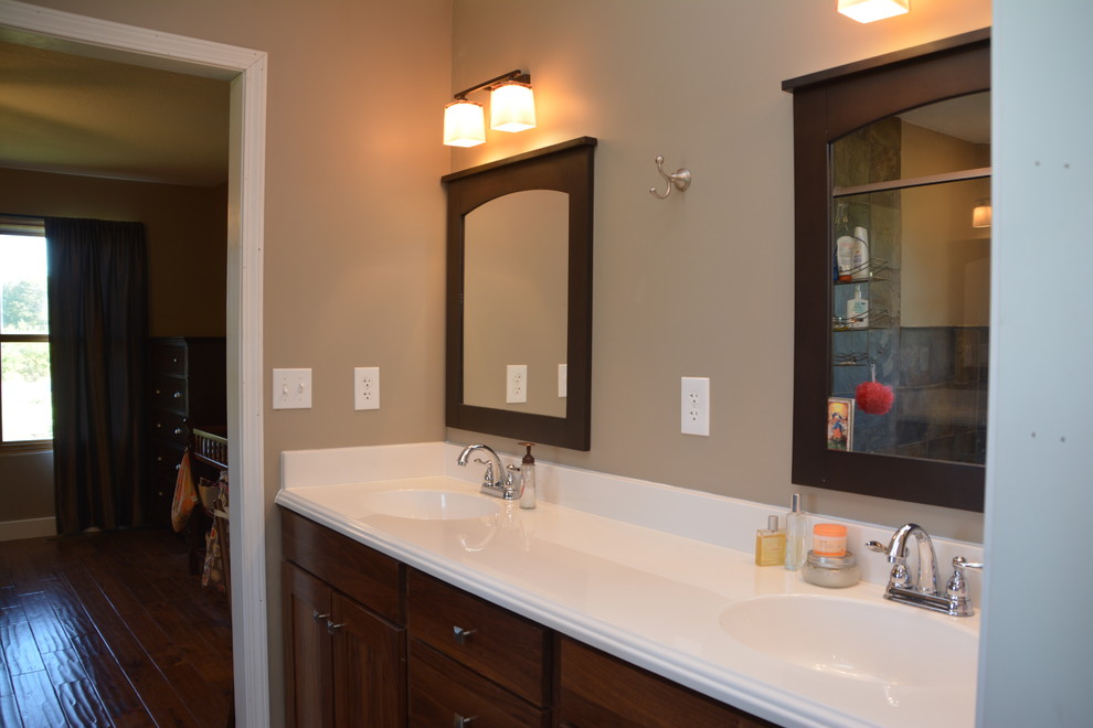 Photo of a medium sized traditional ensuite bathroom in Kansas City with flat-panel cabinets, dark wood cabinets, a built-in bath, a shower/bath combination, beige tiles, black tiles, brown tiles, grey tiles, stone tiles, beige walls, medium hardwood flooring, a submerged sink and solid surface worktops.