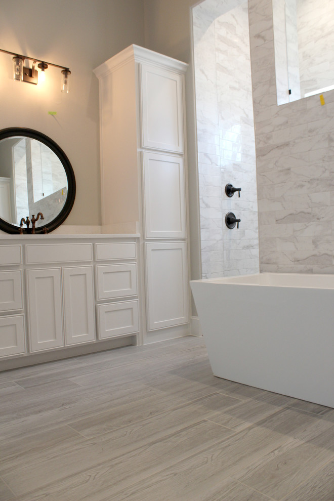 ダラスにある高級な広いトランジショナルスタイルのおしゃれなマスターバスルーム (インセット扉のキャビネット、白いキャビネット、置き型浴槽、ダブルシャワー、分離型トイレ、白いタイル、セラミックタイル、グレーの壁、磁器タイルの床、オーバーカウンターシンク、グレーの床、オープンシャワー、白い洗面カウンター) の写真