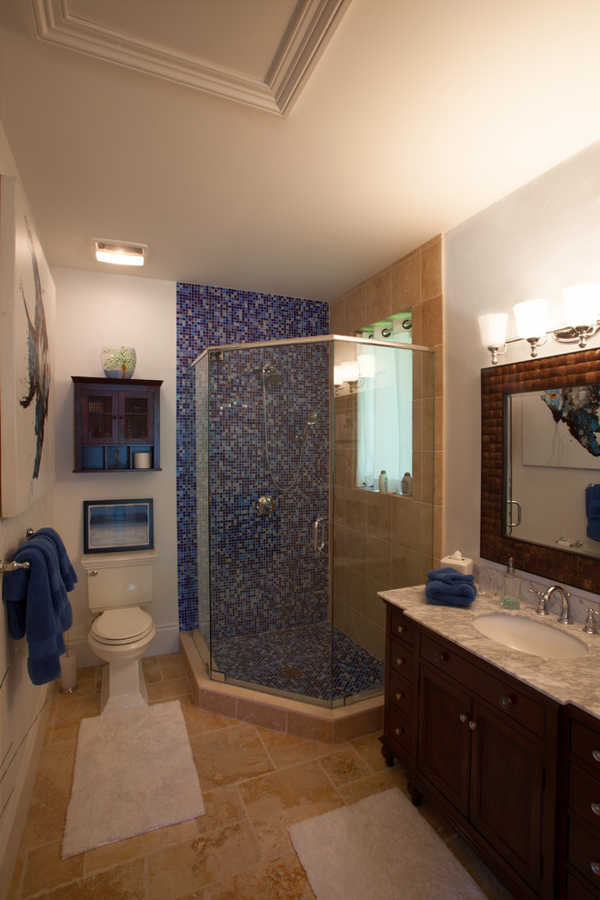 Inspiration for a large tropical master blue tile and mosaic tile travertine floor and beige floor corner shower remodel in Miami with recessed-panel cabinets, dark wood cabinets, a two-piece toilet, white walls, a drop-in sink, granite countertops and a hinged shower door