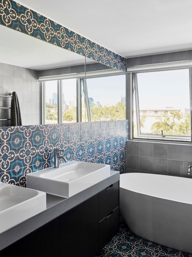 На фото: ванная комната в современном стиле с плоскими фасадами, черными фасадами, отдельно стоящей ванной, синей плиткой, настольной раковиной, синим полом, серой столешницей, тумбой под две раковины и подвесной тумбой с