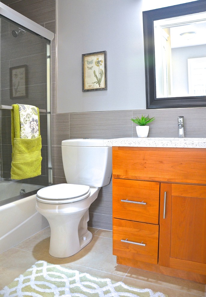 Inredning av ett modernt litet en-suite badrum, med luckor med infälld panel, skåp i mellenmörkt trä, bänkskiva i kvartsit, en dusch/badkar-kombination, en toalettstol med hel cisternkåpa, grå kakel, porslinskakel, grå väggar och klinkergolv i porslin