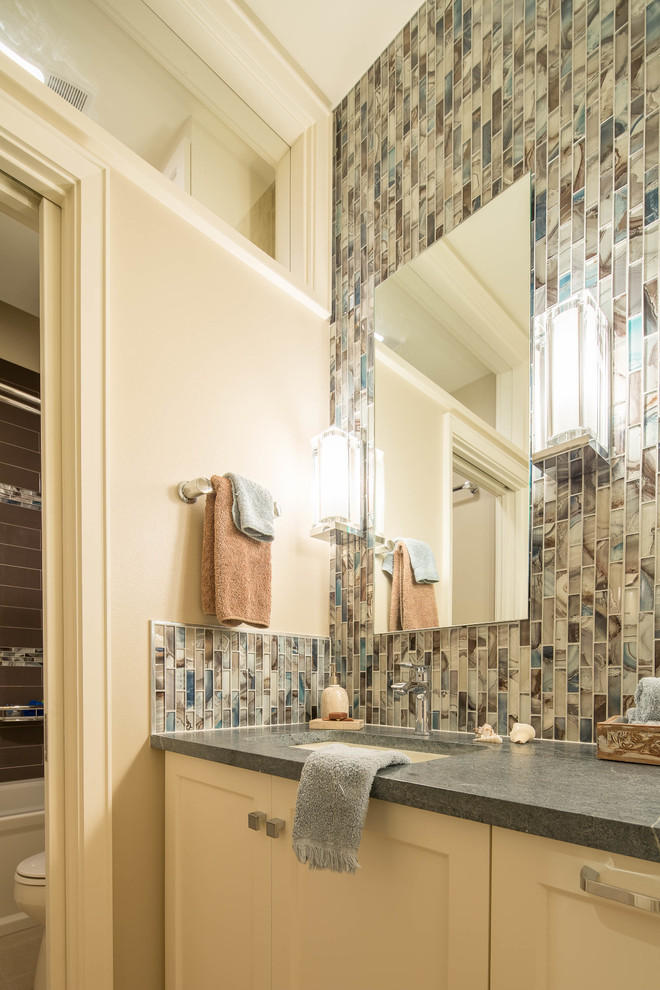 Mid-sized beach style master multicolored tile and glass tile porcelain tile bathroom photo in Austin with recessed-panel cabinets, white cabinets, a two-piece toilet, beige walls, an undermount sink and soapstone countertops