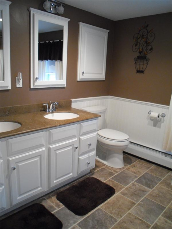 This is an example of a medium sized traditional shower room bathroom in Bridgeport with raised-panel cabinets, white cabinets, an alcove bath, a shower/bath combination, a two-piece toilet, beige tiles, stone tiles, brown walls, porcelain flooring, a submerged sink and solid surface worktops.
