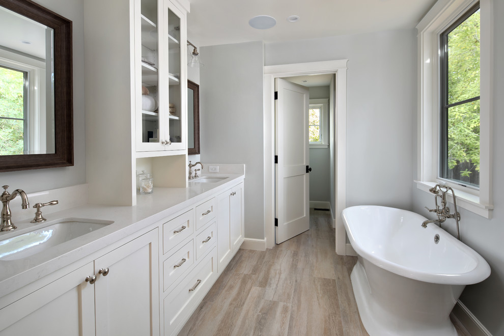 Inspiration for a large traditional ensuite bathroom in San Francisco with shaker cabinets, white cabinets, a freestanding bath, an alcove shower, a two-piece toilet, white walls, light hardwood flooring, a built-in sink, solid surface worktops, beige floors, a hinged door and white worktops.