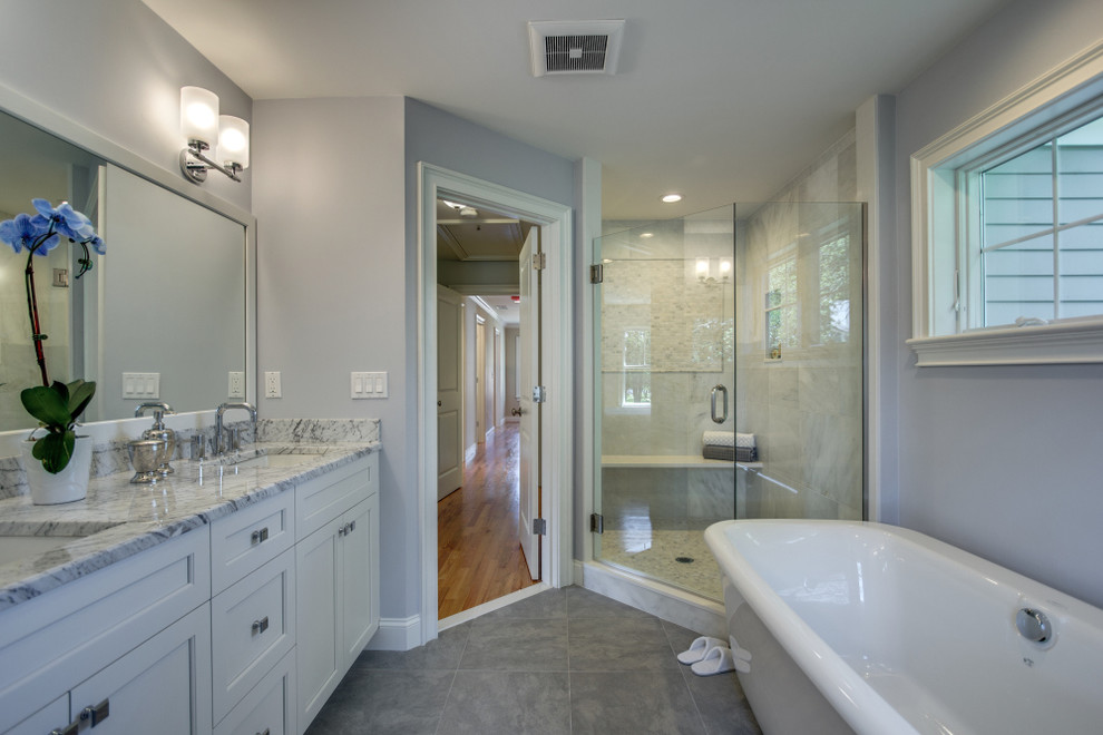 На фото: большая главная ванная комната в классическом стиле с врезной раковиной, белыми фасадами, мраморной столешницей, отдельно стоящей ванной, угловым душем, каменной плиткой, серыми стенами и полом из керамической плитки