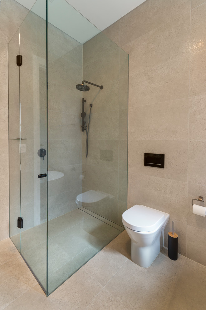 Design ideas for a large contemporary ensuite bathroom in Sydney with flat-panel cabinets, medium wood cabinets, a freestanding bath, a walk-in shower, a two-piece toilet, beige tiles, ceramic tiles, beige walls, ceramic flooring, a vessel sink, engineered stone worktops, beige floors, a hinged door and white worktops.