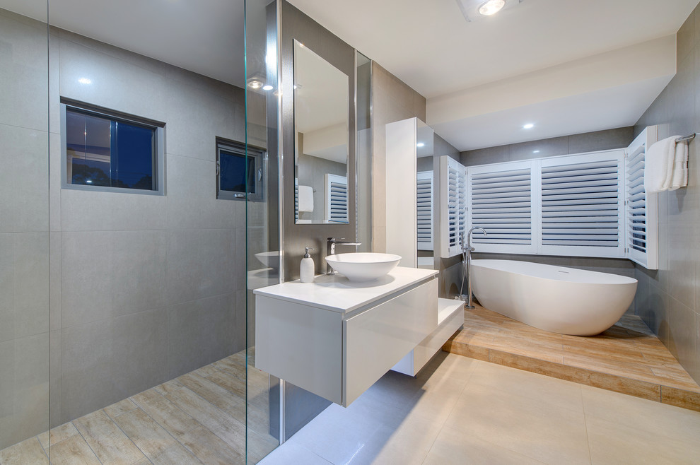 Ejemplo de cuarto de baño actual con lavabo sobreencimera, armarios con paneles lisos, puertas de armario blancas, bañera exenta y baldosas y/o azulejos grises