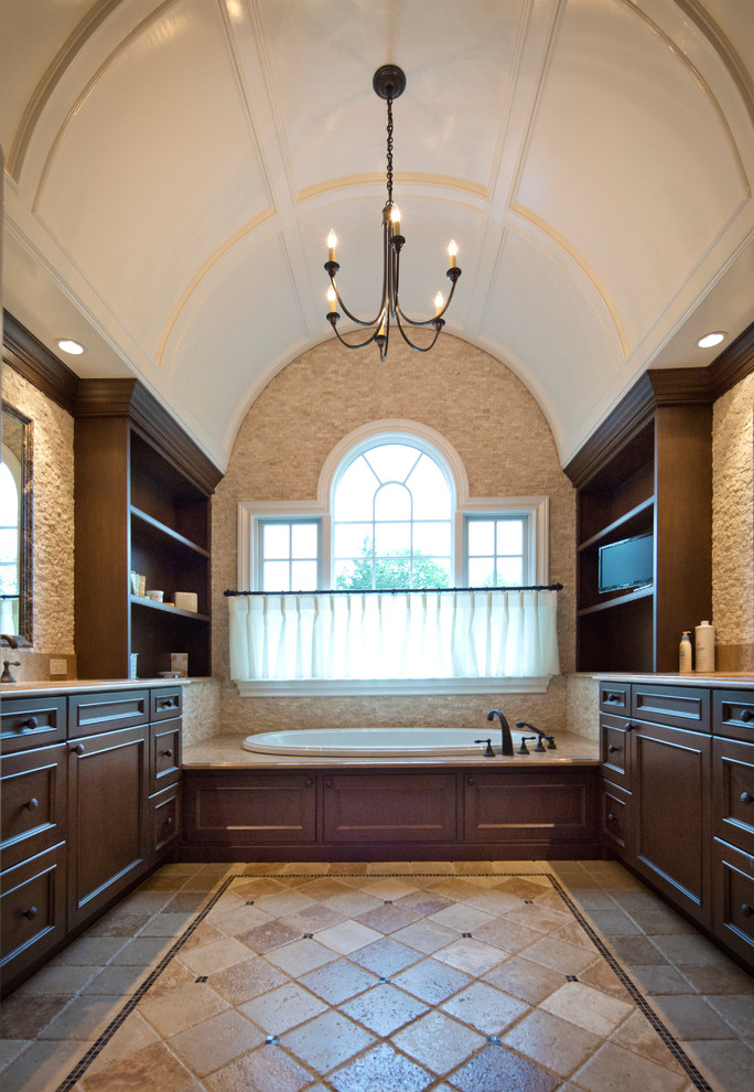 На фото: большая главная ванная комната в классическом стиле с фасадами с декоративным кантом, темными деревянными фасадами, накладной ванной, коричневой плиткой, каменной плиткой, коричневыми стенами, полом из травертина, врезной раковиной и коричневым полом с