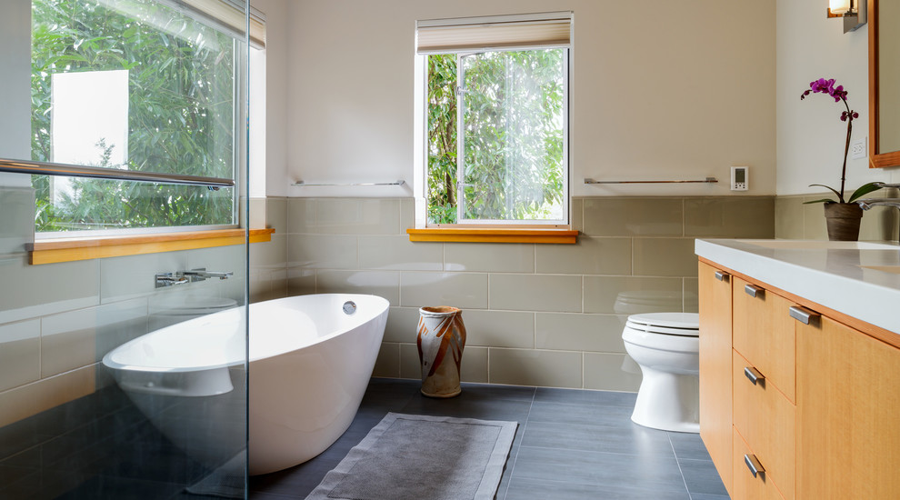 Foto på ett funkis vit badrum, med släta luckor, skåp i mellenmörkt trä, ett fristående badkar, beige kakel, vita väggar och grått golv
