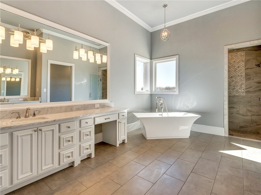 Идея дизайна: большая главная ванная комната в современном стиле с фасадами с выступающей филенкой, белыми фасадами, отдельно стоящей ванной, серыми стенами, полом из керамической плитки, врезной раковиной, мраморной столешницей и коричневым полом