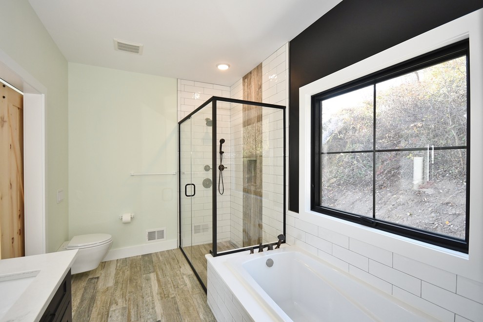 Inspiration for a medium sized traditional ensuite bathroom in Other with recessed-panel cabinets, black cabinets, a built-in bath, a corner shower, a two-piece toilet, white tiles, metro tiles, grey walls, medium hardwood flooring, a submerged sink, quartz worktops, brown floors, a hinged door and white worktops.