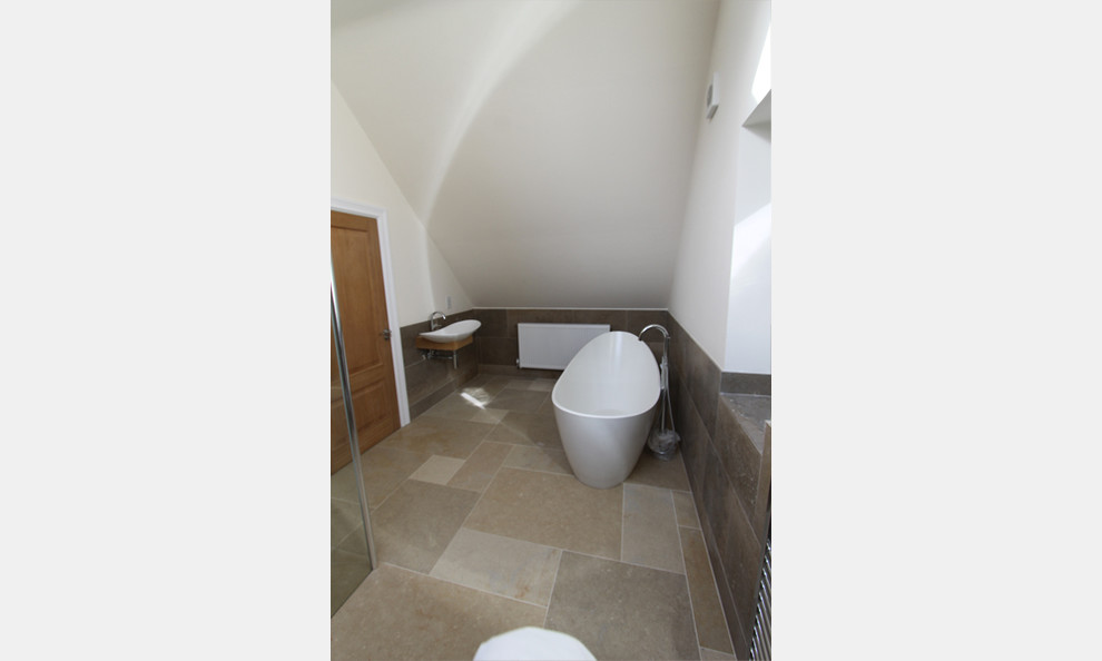 Inredning av ett amerikanskt en-suite badrum, med ett fristående badkar, en öppen dusch, en toalettstol med hel cisternkåpa, beige kakel, stenkakel, vita väggar, kalkstensgolv och ett väggmonterat handfat