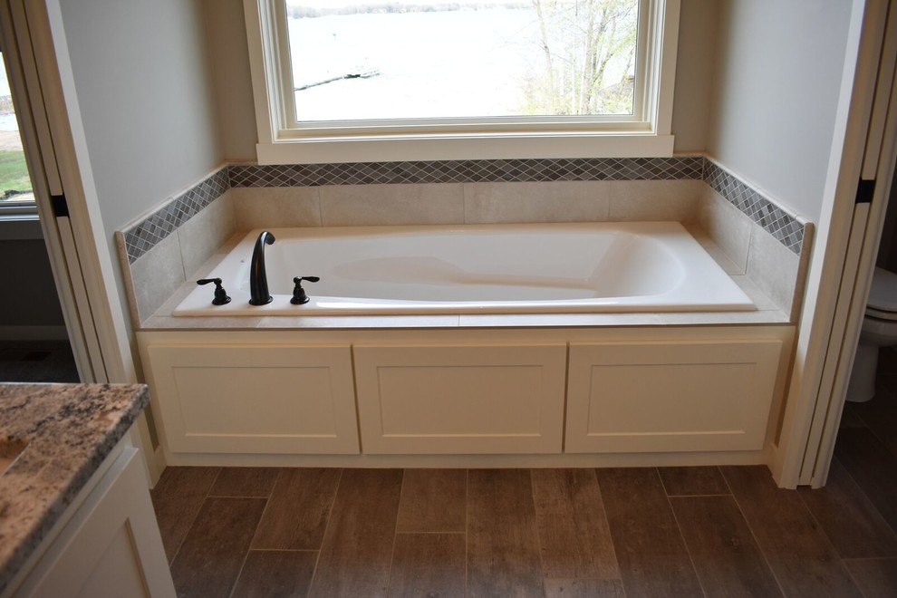 Inspiration for a medium sized traditional ensuite bathroom in Minneapolis with shaker cabinets, white cabinets, a built-in bath, a two-piece toilet, beige tiles, ceramic tiles, grey walls, porcelain flooring, a submerged sink, granite worktops and brown floors.