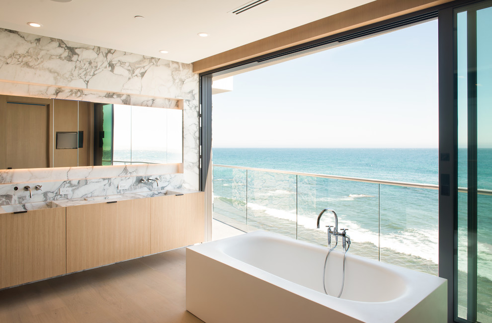 Foto di una stanza da bagno contemporanea con ante in legno chiaro, vasca freestanding, lavabo integrato e ante lisce