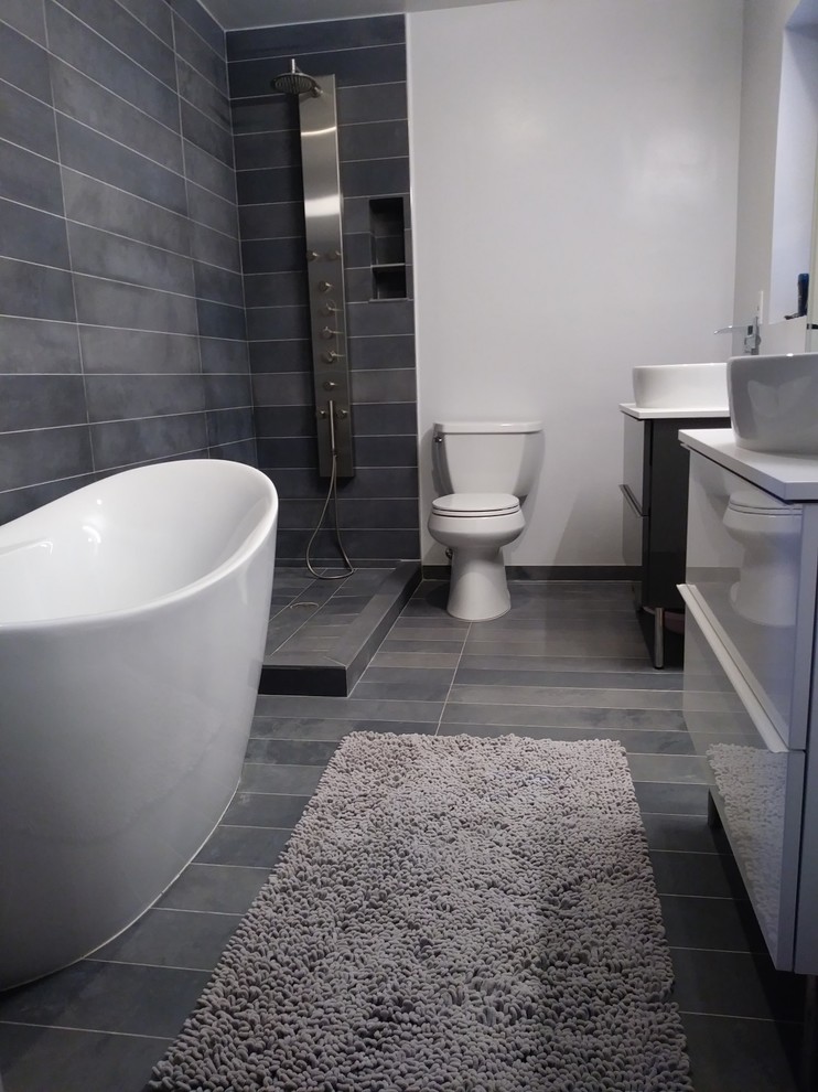 Idéer för att renovera ett mellanstort funkis en-suite badrum, med släta luckor, vita skåp, ett fristående badkar, en öppen dusch, en toalettstol med separat cisternkåpa, grå kakel, porslinskakel, vita väggar, klinkergolv i porslin, ett fristående handfat, laminatbänkskiva, grått golv och med dusch som är öppen