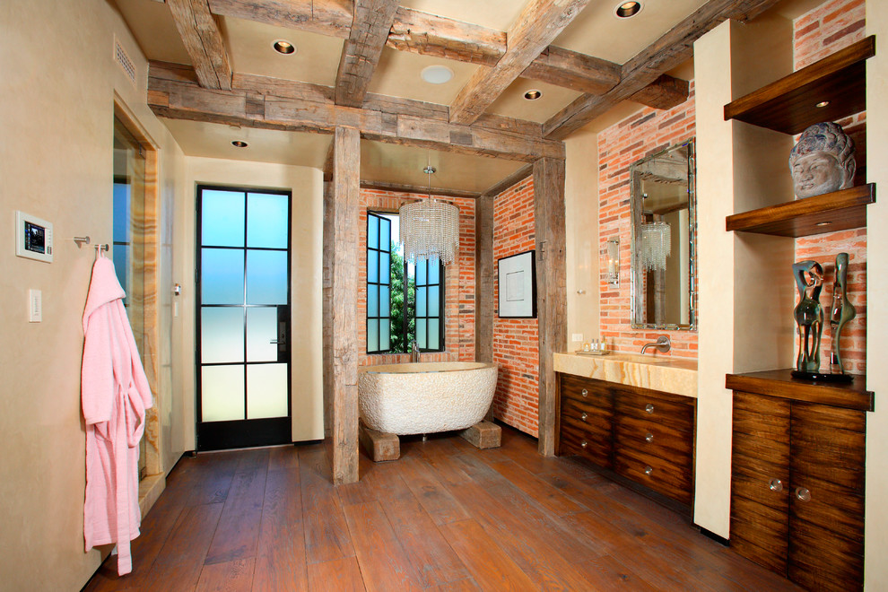 Modelo de cuarto de baño principal mediterráneo con puertas de armario de madera en tonos medios, bañera exenta, encimera de piedra caliza, armarios con paneles lisos, suelo de madera en tonos medios y lavabo integrado