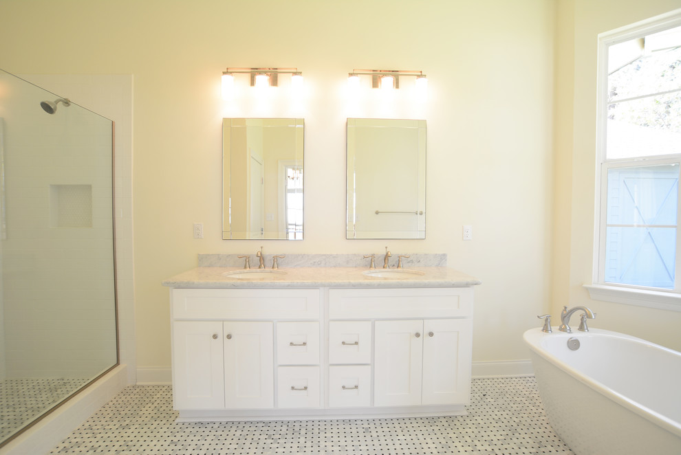 Diseño de cuarto de baño principal de estilo americano de tamaño medio con lavabo bajoencimera, armarios estilo shaker, puertas de armario blancas, encimera de mármol, bañera exenta, ducha doble, sanitario de una pieza, baldosas y/o azulejos blancos y suelo de mármol