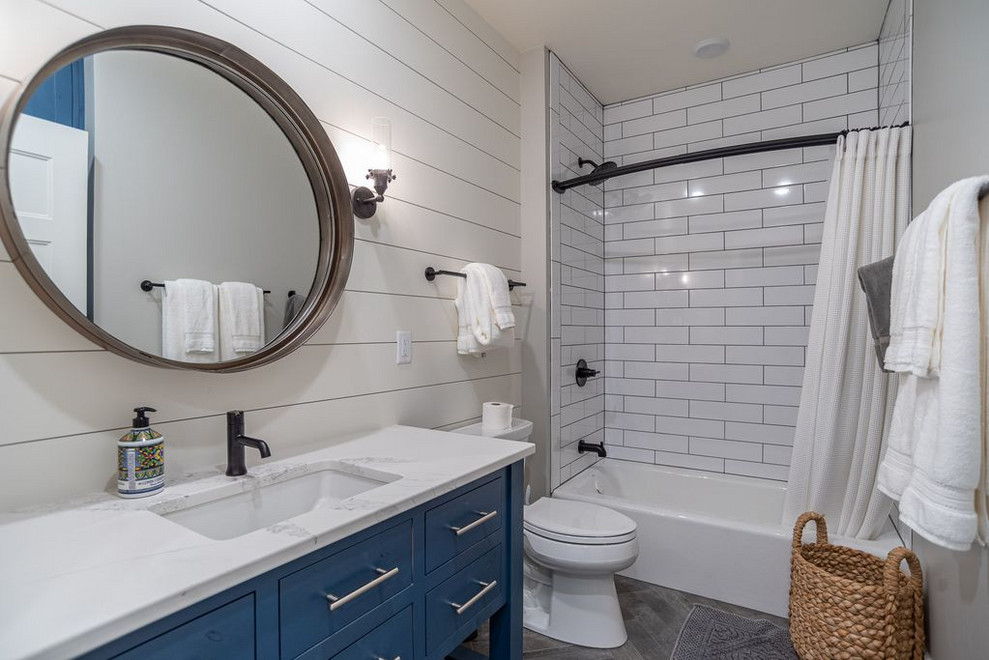 Foto på ett mellanstort funkis gul badrum, med möbel-liknande, blå skåp, ett badkar i en alkov, en dusch/badkar-kombination, en toalettstol med separat cisternkåpa, vit kakel, stenkakel, vita väggar, klinkergolv i porslin, ett undermonterad handfat, bänkskiva i kvarts, grått golv och med dusch som är öppen