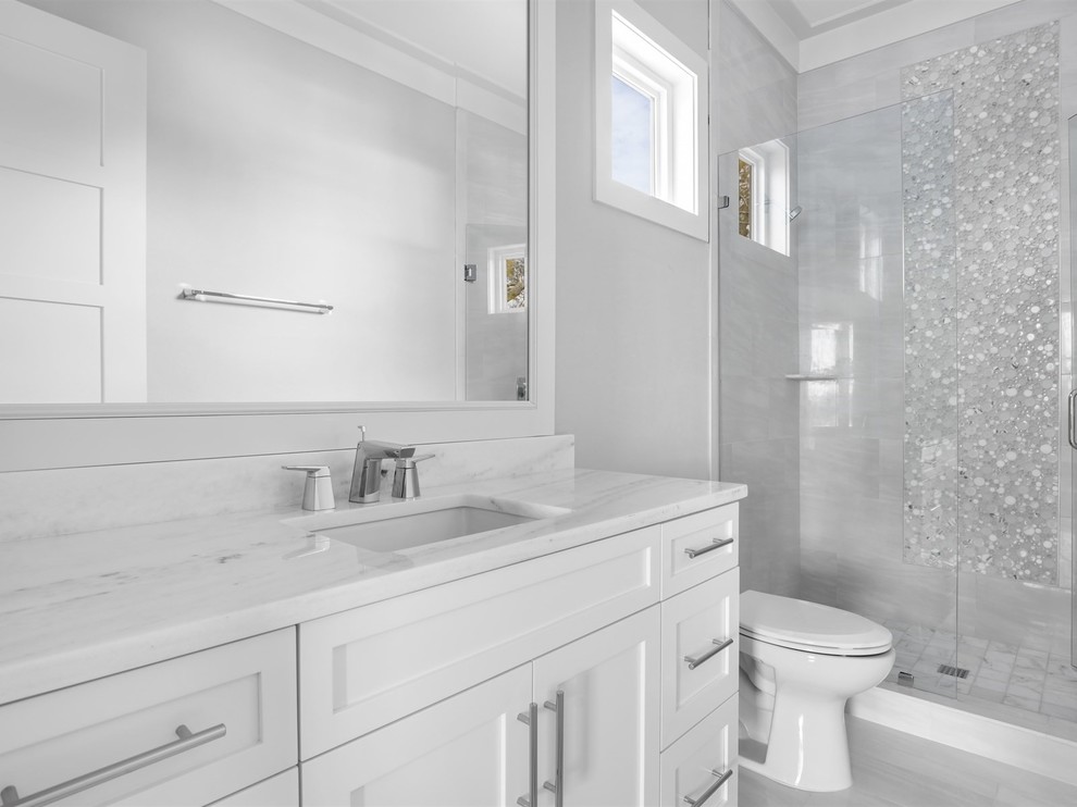 На фото: большая главная ванная комната в стиле неоклассика (современная классика) с фасадами в стиле шейкер, белыми фасадами, душем в нише, раздельным унитазом, серой плиткой, белой плиткой, мраморной плиткой, белыми стенами, мраморным полом, врезной раковиной, мраморной столешницей, белым полом и душем с распашными дверями