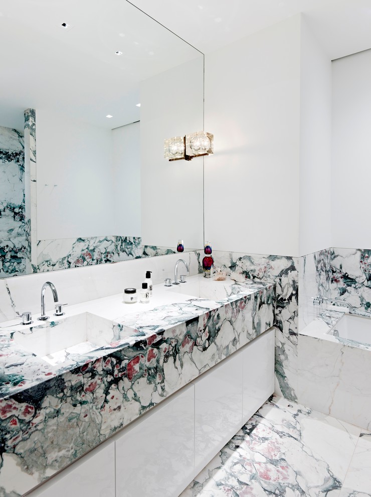 Cette image montre une salle de bain design avec un lavabo intégré, un placard à porte plane, des portes de placard blanches, une baignoire encastrée, un carrelage multicolore, un mur blanc et du carrelage en marbre.