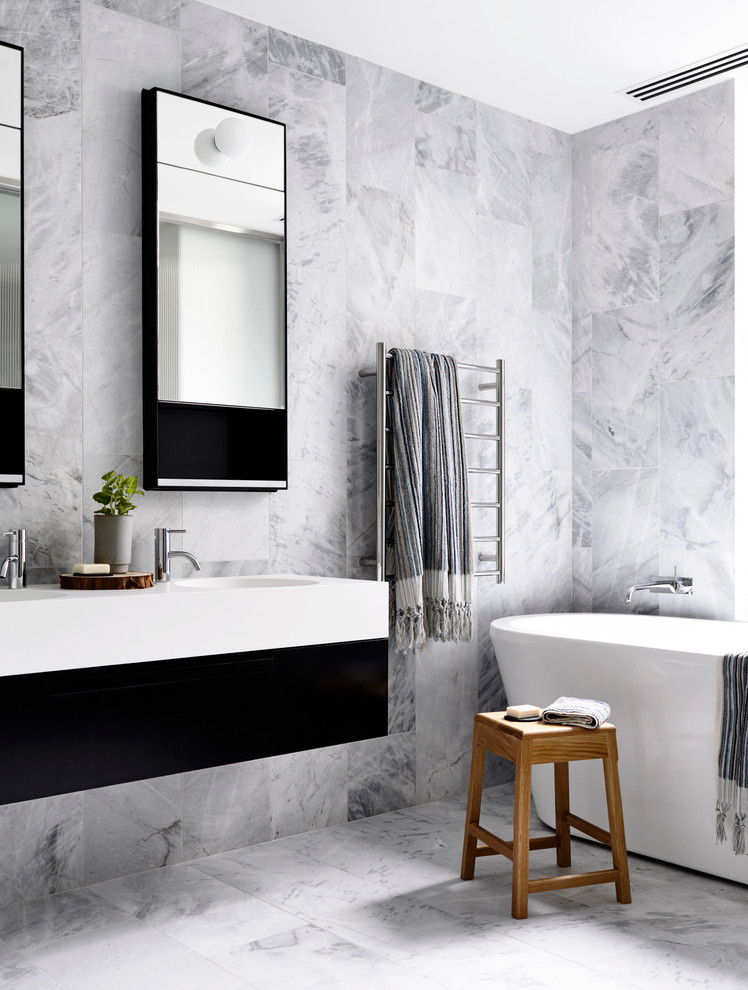 This is an example of a contemporary bathroom in New York with flat-panel cabinets, black cabinets, a freestanding bath, white tiles and an integrated sink.