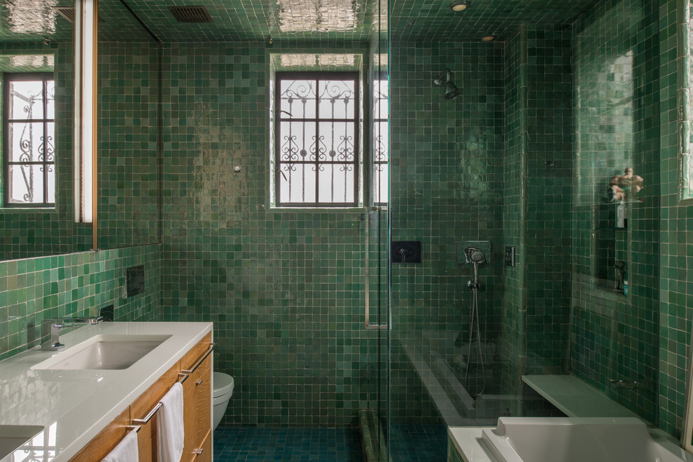 Eklektisches Badezimmer mit flächenbündigen Schrankfronten, hellbraunen Holzschränken, Einbaubadewanne, Eckdusche, grünen Fliesen, Unterbauwaschbecken, grünem Boden, Falttür-Duschabtrennung und weißer Waschtischplatte in New York