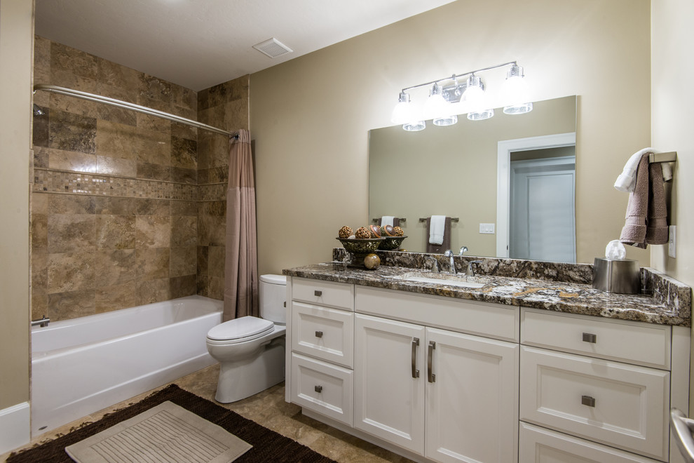 Medium sized traditional shower room bathroom in Salt Lake City with a built-in bath, a shower/bath combination, a one-piece toilet, brown tiles, beige walls, a submerged sink, granite worktops, stone tiles, travertine flooring, white cabinets and recessed-panel cabinets.