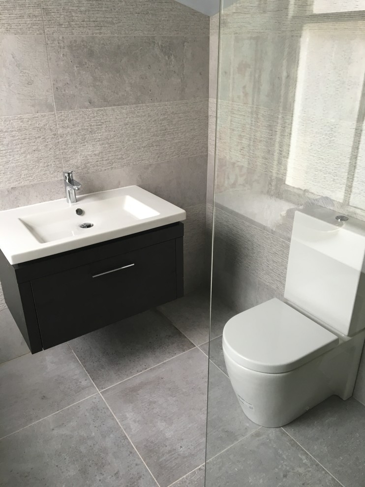 Cette image montre une salle de bain urbaine avec un espace douche bain, un carrelage gris, des carreaux de porcelaine, un mur gris, un sol en carrelage de porcelaine et un lavabo suspendu.
