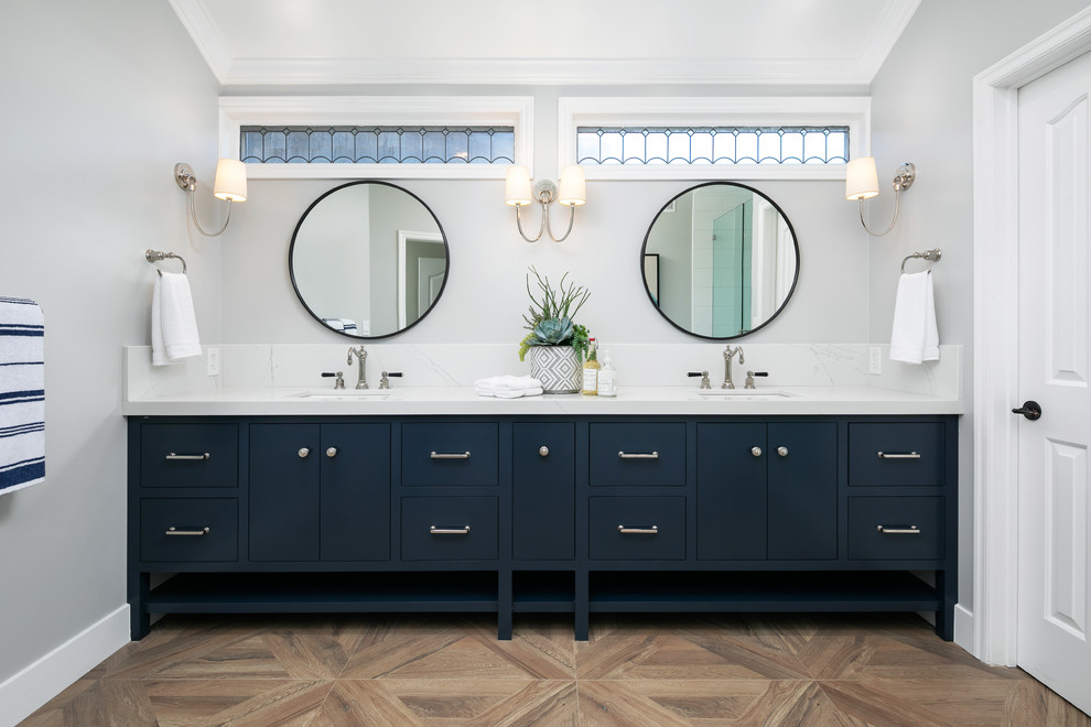 На фото: главная ванная комната в морском стиле с плоскими фасадами, синими фасадами, серыми стенами, врезной раковиной, коричневым полом, белой столешницей и зеркалом с подсветкой