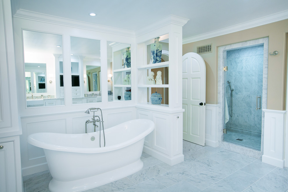 Inspiration for a large traditional ensuite bathroom in Orange County with beaded cabinets, white cabinets, marble worktops, a freestanding bath, white tiles, beige walls and marble flooring.