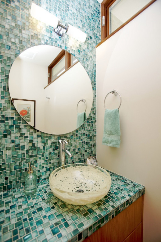 Réalisation d'une salle de bain minimaliste en bois clair avec un placard à porte plane, un carrelage bleu, un carrelage en pâte de verre, un mur blanc, un sol en carrelage de céramique, une vasque et un plan de toilette en verre.