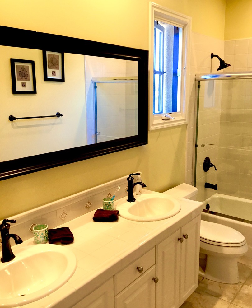 Foto di una stanza da bagno padronale mediterranea di medie dimensioni con ante con bugna sagomata, ante bianche, vasca ad angolo, vasca/doccia, WC monopezzo, piastrelle in ceramica, pareti gialle, lavabo da incasso e top piastrellato