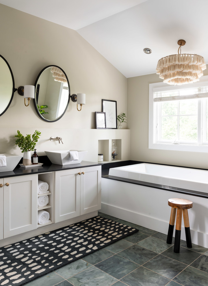 Immagine di una stanza da bagno costiera con ante in stile shaker, ante bianche, vasca da incasso, pareti beige, lavabo a bacinella, pavimento grigio e top nero