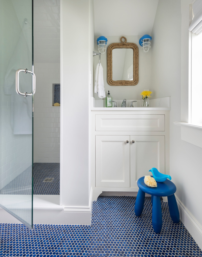 Maritim inredning av ett badrum för barn, med luckor med infälld panel, vita skåp, en dusch i en alkov, vit kakel, tunnelbanekakel, grå väggar och blått golv