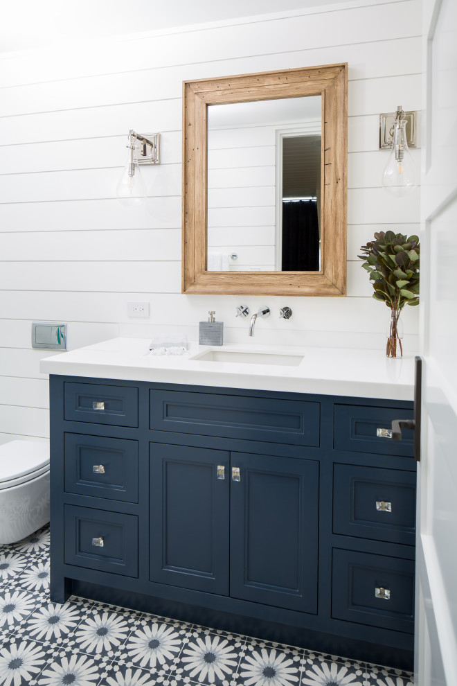Photo of an expansive nautical ensuite bathroom in Orange County with recessed-panel cabinets, blue cabinets, an alcove shower, white tiles, white walls, a built-in sink, a hinged door and grey worktops.