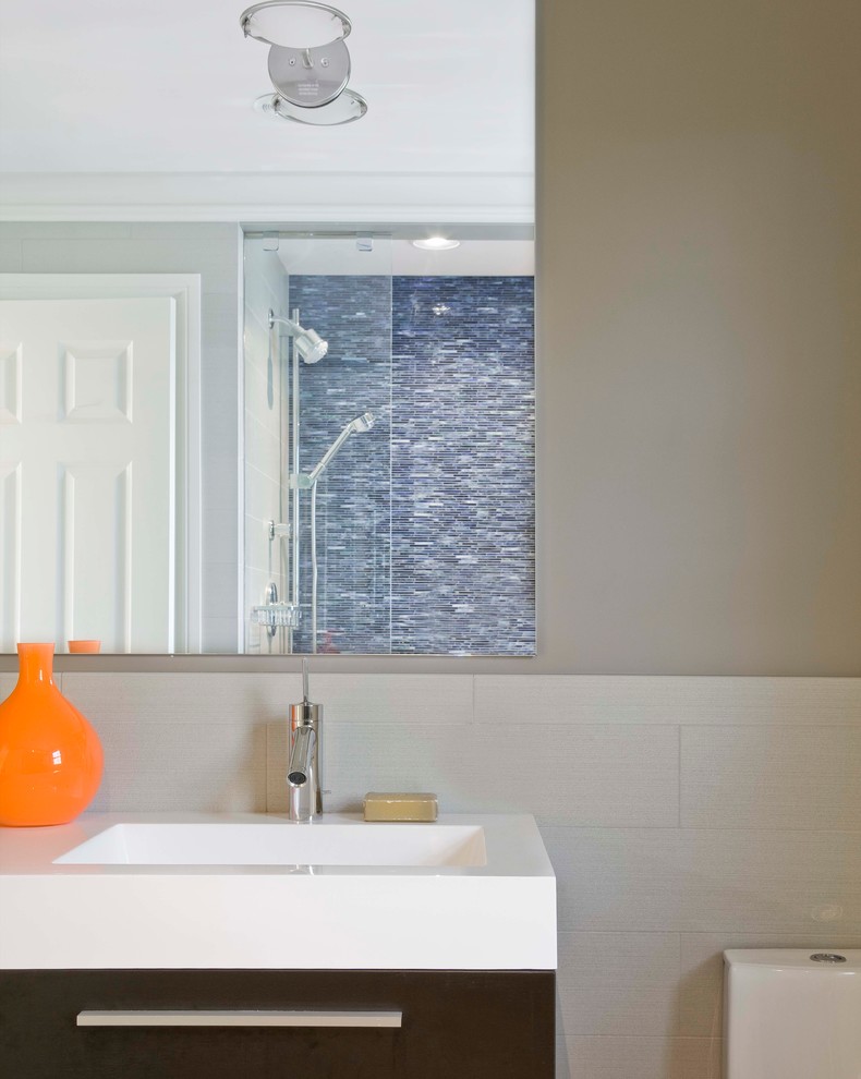 Example of a mid-sized trendy 3/4 blue tile and matchstick tile alcove shower design in Boston with flat-panel cabinets, dark wood cabinets, a one-piece toilet, beige walls, an integrated sink, solid surface countertops, a hinged shower door and white countertops