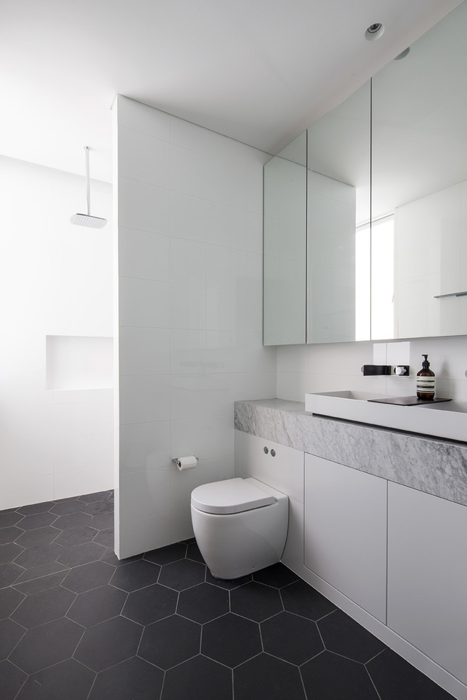 This is an example of a medium sized contemporary shower room bathroom in Sydney with flat-panel cabinets, white cabinets, a built-in bath, an alcove shower, a wall mounted toilet, white tiles, ceramic tiles, white walls, ceramic flooring, a built-in sink and marble worktops.
