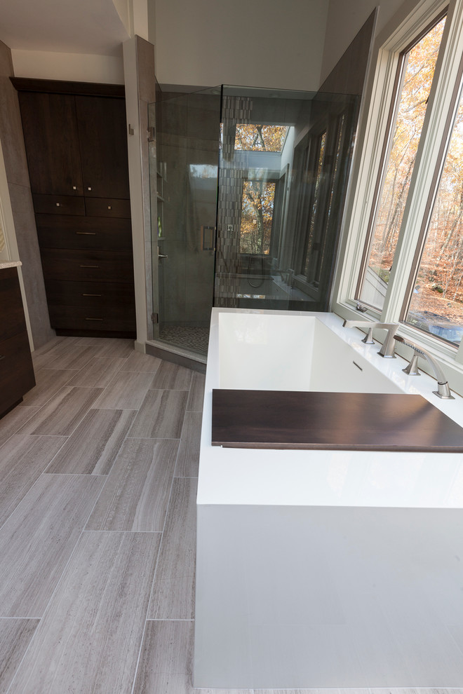 Design ideas for a large modern ensuite bathroom in New York with flat-panel cabinets, brown cabinets, a freestanding bath, a corner shower, a two-piece toilet, grey tiles, porcelain tiles, grey walls, travertine flooring, a submerged sink, recycled glass worktops, grey floors and a hinged door.