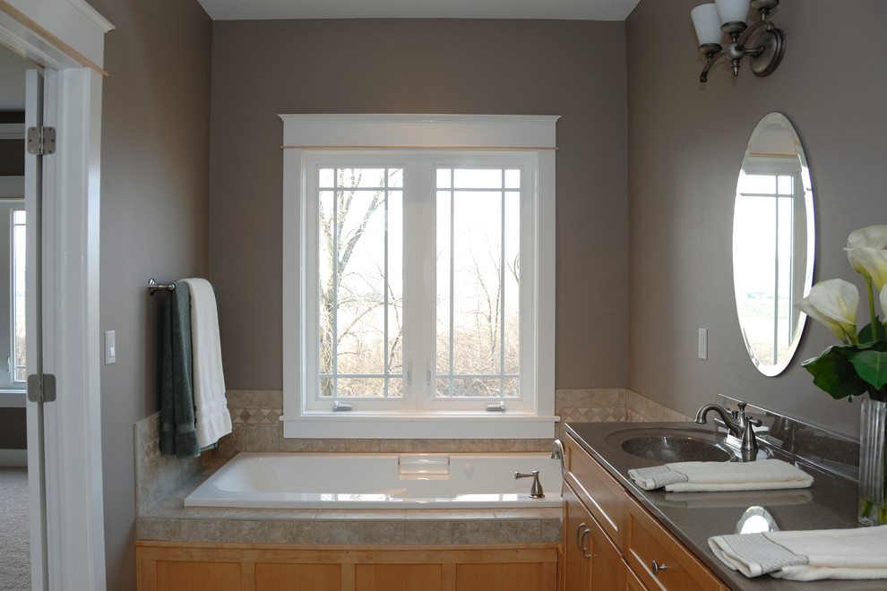 Cette image montre une salle de bain principale traditionnelle en bois brun de taille moyenne avec un placard à porte shaker, une baignoire en alcôve, un carrelage beige, des carreaux de céramique, un mur gris, un lavabo intégré et un plan de toilette en surface solide.