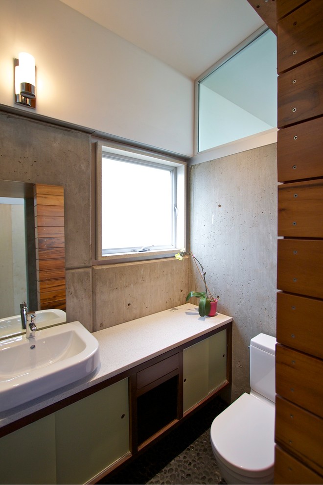Foto på ett funkis badrum, med ett fristående handfat, släta luckor, gröna skåp, en toalettstol med separat cisternkåpa, grå väggar och klinkergolv i småsten
