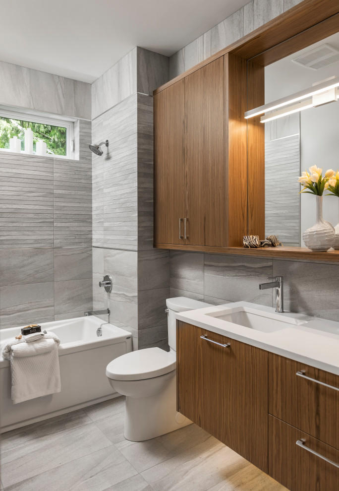 Tub/shower combo - mid-sized contemporary gray tile gray floor and single-sink tub/shower combo idea in Other with flat-panel cabinets, medium tone wood cabinets, a two-piece toilet, an undermount sink, quartz countertops, white countertops, gray walls and a floating vanity