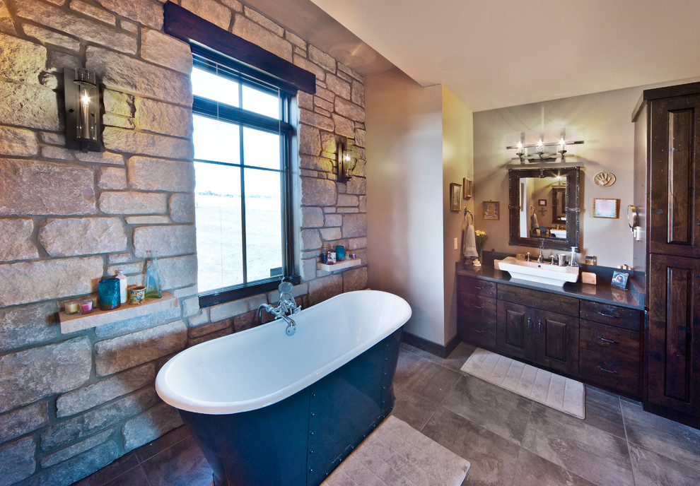 Aménagement d'une salle de bain principale montagne en bois foncé avec une vasque, un placard avec porte à panneau surélevé, un plan de toilette en quartz, une baignoire indépendante, un carrelage gris et des carreaux de céramique.