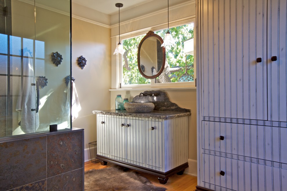 Corner shower - mid-sized eclectic master multicolored tile and pebble tile medium tone wood floor corner shower idea in San Diego with beaded inset cabinets, distressed cabinets, a two-piece toilet, beige walls, a vessel sink and granite countertops