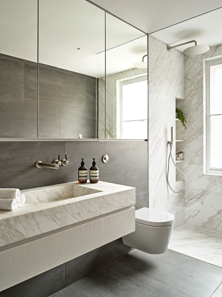 Idéer för ett mellanstort modernt vit badrum, med vita skåp, en vägghängd toalettstol, grå kakel, vit kakel, keramikplattor, marmorbänkskiva, grått golv, med dusch som är öppen, släta luckor, en kantlös dusch och ett integrerad handfat