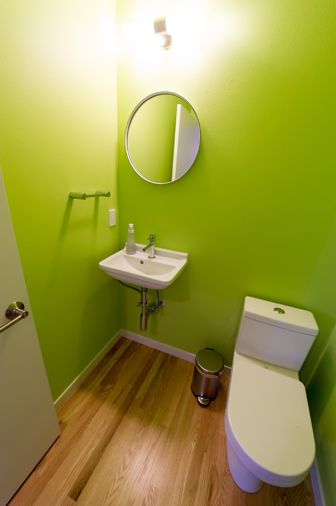 Imagen de aseo minimalista pequeño con sanitario de una pieza, baldosas y/o azulejos verdes, paredes blancas, suelo de madera clara, lavabo suspendido y suelo marrón