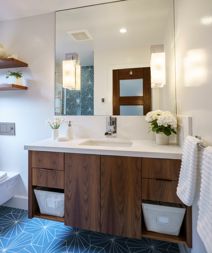 Inredning av ett modernt litet badrum för barn, med släta luckor, skåp i mellenmörkt trä, en vägghängd toalettstol, blå kakel, cementkakel, vita väggar, klinkergolv i keramik, ett undermonterad handfat och bänkskiva i kvarts