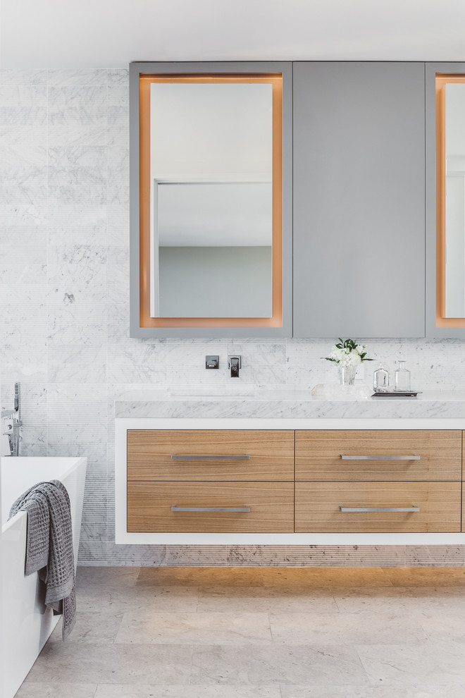 Réalisation d'une salle de bain principale design en bois clair avec un placard à porte plane, une baignoire indépendante et un lavabo encastré.