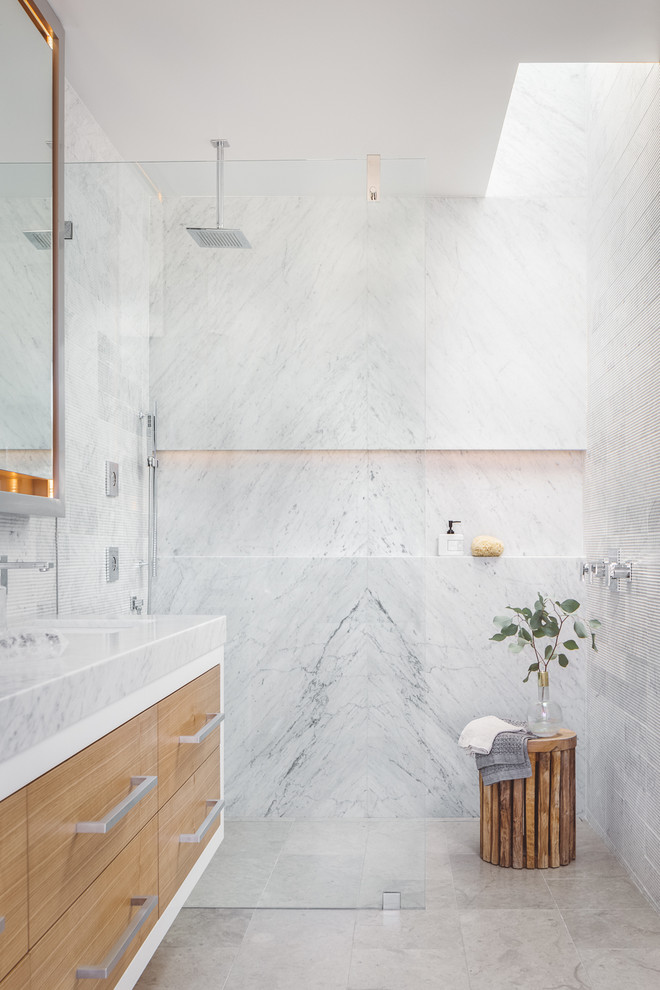 Cette photo montre une salle de bain tendance en bois clair avec un placard à porte plane, un carrelage blanc, des dalles de pierre, un sol en marbre, un lavabo encastré, un plan de toilette en marbre, une douche à l'italienne, aucune cabine et une niche.