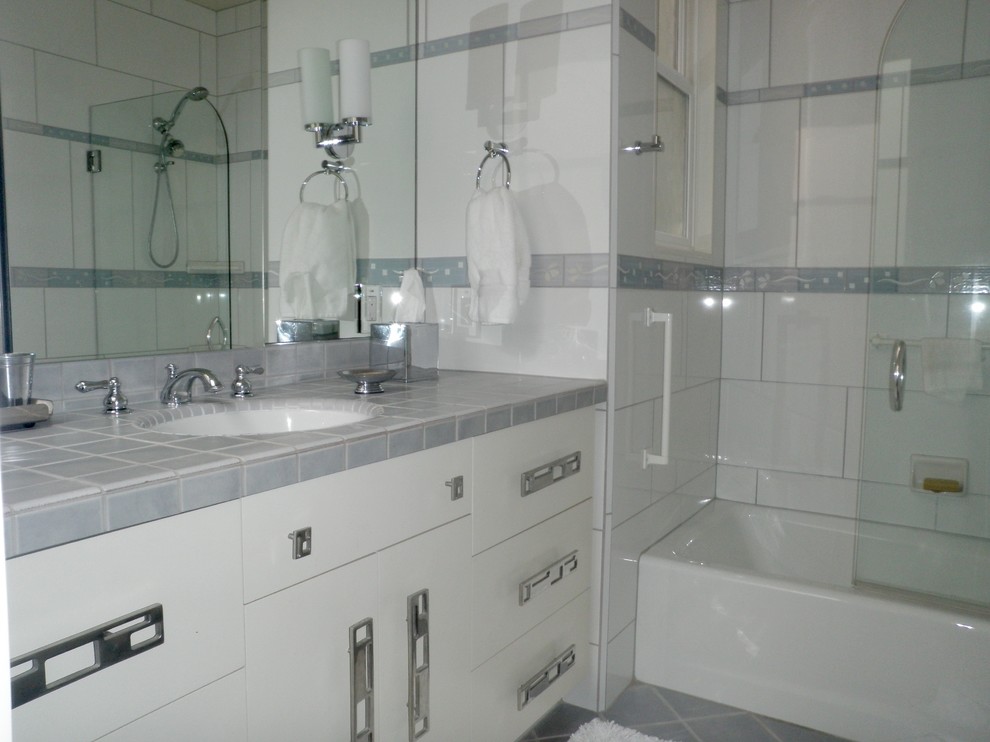 Photo of a medium sized classic ensuite bathroom in San Francisco with flat-panel cabinets, white cabinets, an alcove bath, a shower/bath combination, white tiles, porcelain tiles, white walls, porcelain flooring, a submerged sink, tiled worktops, grey floors and a hinged door.