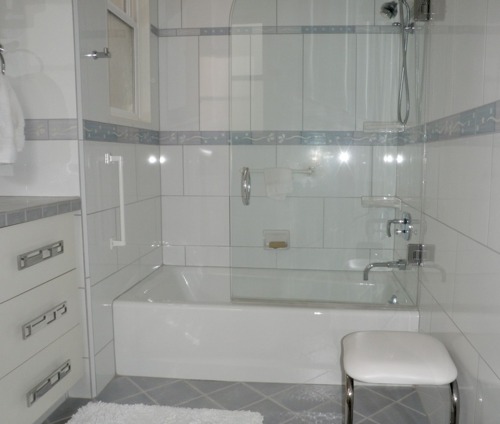 Идея дизайна: главная ванная комната среднего размера в стиле неоклассика (современная классика) с плоскими фасадами, белыми фасадами, ванной в нише, душем над ванной, белой плиткой, керамогранитной плиткой, белыми стенами, полом из керамогранита, врезной раковиной, столешницей из плитки, серым полом и душем с распашными дверями